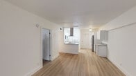 This single-floor residence offers a clean, modern aesthetic defined by an open-concept layout and light hardwood flooring that flows seamlessly throughout the living areas and bedrooms. The kitchen serves as a standout centerpiece, showcasing granite countertops, flat-front white cabinetry, and a full suite of stainless steel appliances including a refrigerator, dishwasher, microwave, and electric range. A striking island-mounted glass and stainless steel range hood adds a bold architectural element, anchoring the kitchen visually while connecting it to the open living space. A peninsula with a sink and additional counter space enhances both functionality and flow. The living area is generously proportioned, bathed in natural light through a large sliding glass door fitted with vertical blinds, offering a bright and airy atmosphere. The bedroom features a window with blinds providing comfortable natural light and ample wall space. The bathroom is tastefully updated with granite countertops, a brushed gold faucet and fixtures, a framed mirror, and a tiled tub-shower combination. Throughout the residence, crisp white walls and a neutral palette create a cohesive, contemporary environment that is both inviting and versatile.