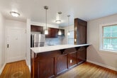 Located at 26 Beaumont Pl, Unit 2G in Newark, NJ, this 2-bedroom, 1-bathroom residence offers a well-organized single-floor layout with a thoughtful mix of classic and updated finishes throughout. Warm-toned hardwood floors run continuously through the bedrooms and living areas, lending a cohesive and inviting character to the entire unit.

The kitchen is a standout feature, showcasing rich dark wood cabinetry, a marble-style tile backsplash, a white countertop breakfast bar with decorative corbels, stainless steel appliances, and pendant lighting overhead. A window adjacent to the kitchen brings in natural light and connects the space to the outdoors.

The spacious primary bedroom comfortably accommodates large furnishings and is brightened by a pair of windows overlooking greenery, complemented by a radiator for efficient heating. The second bedroom is similarly well-proportioned, featuring its own window with natural light and gleaming hardwood floors. Both rooms include access to closets via clean white paneled doors.

The bathroom is elegantly finished with floor-to-ceiling marble-look porcelain tile, a soaking tub with shower, a dark-cabinet vanity, and a window providing natural ventilation. A connecting hallway ties all rooms together, completing this functional and attractive urban residence.