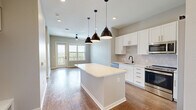 Located at 410 E Pikes Peak Ave in Colorado Springs, CO, this well-appointed 1-bedroom, 1-bathroom unit offers a thoughtfully designed open-concept layout across a single floor. The kitchen serves as a central highlight, featuring white shaker cabinetry with gold and matte black hardware, a classic subway tile backsplash, stainless steel appliances including a refrigerator, range, microwave, and dishwasher, and a large center island with a light quartz countertop illuminated by striking black pendant lights. Rich hardwood-style flooring flows through the kitchen and living areas, while recessed lighting adds a clean, modern finish. The living room is bright and airy, with a ceiling fan, large windows, and a glass door that invites natural light and offers elevated views of the Colorado Springs cityscape and mountain backdrop. The bedroom is carpeted for comfort, features its own large window with scenic views, and connects to a generous walk-in closet outfitted with built-in shelving and double hanging rods. The bathroom is elegantly finished with large-format tile flooring, a dual-sink white vanity with matte black fixtures, a wide mirror with sconce lighting, and a glass-enclosed walk-in shower with white tile surround.