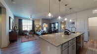 This single-story, two-bedroom, two-bathroom residence offers a thoughtfully designed open-concept layout that promotes a seamless flow between living spaces. Wood-style plank flooring runs throughout the main living areas, lending warmth and continuity to the design.

The kitchen serves as a central hub, anchored by a large granite-topped island with an undermount sink and pendant lighting above. Gray shaker-style cabinetry lines the walls, complemented by a decorative tile backsplash and stainless steel appliances, including a range and over-the-range microwave. The kitchen opens directly into the living area, which features a ceiling fan, multiple windows admitting natural light, and views into an adjacent dining space defined by a stylish glass-panel partition.

Each bedroom is carpeted and includes walk-in closet space and windows with blinds. One bedroom is served by a full bathroom featuring a tub/shower combination, wood-style flooring, and granite-topped vanity cabinetry. The second bathroom mirrors this aesthetic and is conveniently accessible from the hallway.

A dedicated laundry room houses a full-size washer and dryer. The overall palette of neutral grays and warm tones creates a cohesive, contemporary ambiance throughout.