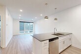 Located at 3003 Leavenworth St in Omaha, Nebraska, this well-appointed one-bedroom, one-bathroom unit offers a clean, modern aesthetic throughout its efficiently designed floor plan. The open-concept kitchen and living area serves as the heart of the unit, featuring a central island with a dark quartz countertop, an undermount double sink, and white shaker cabinetry. Stainless steel appliances — including a refrigerator, range, microwave, and dishwasher — complete the kitchen. Stylish globe pendant lights hang above the island, adding a contemporary touch. Light wood-style flooring flows through the main living area, which benefits from recessed lighting and a large window that frames views of the surrounding Omaha cityscape. The bedroom is comfortably sized, finished with plush carpet, a ceiling fan, and a generous window that brings in natural light and additional urban views. A dedicated closet provides convenient storage. The bathroom features a combined tub and shower, a white vanity with dark countertop, and matching hardware finishes consistent with the rest of the unit. The overall design is bright, neutral, and move-in ready, reflecting a modern urban living experience.