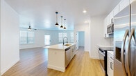 Located at 5815 S Elk Way in Aurora, Colorado, this single-story 2-bedroom, 3-bathroom home showcases a clean, modern design with an open and airy feel. Light wood-tone flooring flows seamlessly throughout, complemented by crisp white walls, black hardware accents, and recessed lighting.

The open-concept kitchen and living area serves as the heart of the home. The kitchen features a large central island with a white quartz countertop, undermount sink, stainless steel appliances including a range, microwave, and refrigerator, white shaker cabinetry, and a subway tile backsplash. A trio of pendant lights adds a stylish focal point above the island. The adjacent living area is generously proportioned, boasting curved walls, multiple windows that invite abundant natural light, a ceiling fan, and direct access to the exterior.

The primary bedroom is a well-sized retreat with curved walls, dual windows, a ceiling fan, and its own dedicated closet space. The second bedroom is bright and comfortable, also featuring a ceiling fan and natural light. A connecting hallway with Shaker-style doors and overhead ventilation ties the layout together efficiently.

The bathrooms are thoughtfully finished with gray large-format tile surrounds on the tub/shower, gray cabinetry, white countertops, and illuminated mirrors with matte black fixtures — offering a polished, contemporary aesthetic throughout.