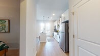 This well-appointed single-floor residence offers a clean, modern aesthetic throughout, characterized by light-toned walls, light wood-style flooring, and an abundance of natural light.

The kitchen serves as a functional centerpiece of the home, featuring white shaker-style cabinetry, granite countertops, a subway tile backsplash, and a full suite of stainless steel appliances including a refrigerator, range, and built-in microwave. A kitchen island with seating provides additional prep space and casual dining, while pendant lighting adds a warm, polished touch. French doors adjacent to the kitchen invite natural light and provide outdoor access.

The living area is generously sized with elevated ceilings and a ceiling fan overhead. A large window dressed with floor-length curtains brings in soft, natural light, creating a welcoming and airy atmosphere.

The bedroom features plush carpeting, a softly lit and cozy feel, and direct access to a spacious walk-in closet equipped with wire shelving for ample storage.

The bathroom includes a full soaking tub with a tiled shower surround, a curved curtain rod, wood-style flooring, and clean, neutral finishes throughout — offering a calm and functional space.