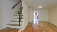 This three-floor home offers a well-organized and practical layout designed for comfortable everyday living. The main level greets you with gleaming hardwood floors that stretch throughout the open living area, lending warmth and a timeless character to the space. A staircase with wooden treads and a sleek black metal railing serves as a central architectural feature, connecting the floors with a clean, classic aesthetic. The open corridor leads naturally toward a bright kitchen, which is visible from the main living area and features wooden cabinetry and standard appliances — a practical and efficient workspace. The white walls throughout provide a neutral, light-filled backdrop that enhances the sense of openness across the main level. The additional floors above expand the living potential of the home, offering further space for bedrooms, offices, or flexible-use rooms. With its polished hardwood flooring, straightforward layout, and well-maintained finishes, this multi-story home balances function with understated charm, making it a solid and adaptable living space suitable for a range of occupants and lifestyles.