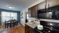 Located at 206 Cedar Branch Ln in Wilmington, NC, this three-floor home offers a thoughtfully designed layout across multiple levels connected by a central staircase. The galley-style kitchen is a standout feature, showcasing rich dark-espresso cabinetry, granite countertops, black appliances including a range, microwave, and refrigerator, and warm hardwood flooring that extends into the adjacent dining and living areas. The dining area benefits from natural light streaming through large windows, complemented by tasteful accent walls in muted blue-gray tones. The living room is an inviting, light-filled space with hardwood floors and a generous window overlooking the outdoors. Multiple bedrooms offer plush carpeting, ceiling fans, and natural light, each with its own character—one features a serene coastal-inspired palette while another offers a bold, dark accent wall. Bathrooms are well-appointed with dark wood vanities, white countertops, large mirrors, and tile flooring. A spacious walk-in closet with built-in wire shelving provides ample storage. The multi-level floor plan, consistent finishes, and coastal-inspired touches throughout give this Wilmington home a comfortable and cohesive aesthetic.