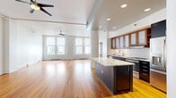 This well-appointed 1-bedroom, 2-bathroom residence offers a thoughtfully designed layout spread across a single, generously sized floor. Rich hardwood floors flow throughout, lending warmth and continuity to every room.

The heart of the home is an expansive open-concept kitchen and living area. The kitchen is a standout, featuring dark lower cabinetry contrasted by warm wood upper cabinets with frosted glass inserts, a white subway tile backsplash, stainless steel appliances including a French door refrigerator and range, and a striking marble-topped center island. The living room is bathed in natural light from large windows and features ceiling fans and recessed lighting overhead.

The bedroom is a comfortable, well-proportioned retreat finished with the same warm hardwood flooring and crisp white walls. It includes dedicated closet space and access to the hallway corridor.

The two bathrooms offer distinct configurations: one features a sleek glass-enclosed walk-in shower with white tile surround and a wood-toned vanity, while the second includes a full soaking tub with a shower and matching white tile. Both are finished with mosaic tile flooring.

Additional hallways and two closets provide practical storage throughout, rounding out this clean, modern, and highly functional living space.