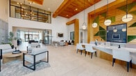 This thoughtfully designed amenity facility spans a single floor and offers a diverse array of spaces united by a cohesive modern aesthetic. The grand entrance lobby immediately impresses with soaring double-height ceilings, warm natural wood beam accents, large-format tile flooring, and dramatic pendant lighting. A living moss wall and built-in reception counter create a polished, welcoming focal point, while floor-to-ceiling glass doors flood the space with natural light and outdoor views.

Multiple living room areas serve distinct purposes throughout the facility. One features a bright, airy dining-lounge configuration with a long communal wood table beneath bold pendant lights and sheer curtains. Another offers an intimate lounge with rich slate-blue walls, channeled leather sectional sofas, and a gold-accented statement chandelier. A game room provides entertainment with a billiards table, arcade basketball, large-screen TVs, and a shiplap ceiling in a playful coastal palette.

Private office spaces offer quiet, focused work environments, each with floor-to-ceiling windows, built-in desks, and soft carpet flooring. A cozy booth-style meeting nook features warm wood-planked walls and upholstered banquette seating for intimate gatherings.

The expansive fitness center rounds out the offering, boasting high ceilings, natural wood columns, mirrored walls, cardio equipment, strength machines, and free weights — all bathed in natural light from clerestory windows.