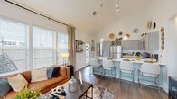 Located at 1110 Kathryn Ryals Rd in Warner Robins, Georgia, this thoughtfully designed single-story home impresses with soaring vaulted ceilings that lend an airy, expansive quality to the open-concept living area. Large windows dressed with linen drapes and plantation blinds flood the space with abundant natural light, highlighting the rich hardwood-style flooring found throughout.

The living room offers a welcoming atmosphere, anchored by a comfortable seating arrangement and a sleek coffee table. It flows seamlessly into the kitchen, which serves as a functional centerpiece of the home. Gray shaker-style cabinetry, white countertops, a subway tile backsplash, and a full suite of stainless steel appliances define the space, while a peninsula with bar seating provides an ideal spot for casual dining. Globe pendant lights add a contemporary touch overhead.

The bedrooms are bright and well-proportioned, each featuring large windows with natural light and ample space for restful retreats. The primary bedroom includes a ceiling fan and connects to a spacious en-suite bathroom featuring dual vanities with gray cabinetry, a glass-enclosed walk-in shower, and hardwood-style flooring. A secondary bathroom mirrors the same refined aesthetic with a single vanity and shower-tub combination. The home's cohesive design and quality finishes make it a comfortable and stylish residence.