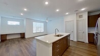 This well-appointed 1-bedroom, 1-bathroom unit offers a thoughtfully designed single-floor layout that maximizes functionality and comfort. The open-concept kitchen and living area forms the heart of the space, anchored by a central kitchen island with a white quartz countertop and undermount sink. The kitchen is fully equipped with stainless steel appliances—including a refrigerator, range, and microwave—complemented by warm wood-toned cabinetry and a classic subway tile backsplash. Recessed lighting and a ceiling fan illuminate the living area, which benefits from natural light streaming through a large window fitted with horizontal blinds. Warm wood-look flooring extends seamlessly throughout the entire unit, creating a cohesive and modern aesthetic against the crisp white walls. The bedroom is a comfortable, well-proportioned retreat featuring a built-in wood-accented desk, making it ideal for both rest and remote work. A large window with outdoor views adds brightness to the room. The bathroom is clean and contemporary, featuring a glass-enclosed walk-in shower with floor-to-ceiling tile surround and modern brushed nickel fixtures. A hallway connects the living spaces to the private areas, completing this efficient and stylish layout.