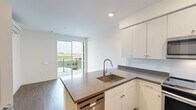 Located at 1547 Pacific Ave in Santa Cruz, California, this modern one-bedroom, one-bathroom residence offers a thoughtfully designed layout with contemporary finishes throughout. The open-concept living and kitchen area is anchored by a central island with stone countertops and an undermount sink, providing both functional workspace and a natural gathering point. The kitchen is fully equipped with stainless steel appliances, including a range, over-the-range microwave, refrigerator, and dishwasher, complemented by floor-to-ceiling white cabinetry offering ample storage. Wood-style flooring runs throughout the unit, adding warmth to the clean, modern aesthetic. Sliding glass doors lead to a private balcony, inviting natural light into the living space and offering outdoor views. The bedroom is a comfortable retreat featuring recessed lighting, a large window, and a walk-in closet. The bathroom is finished with a full tub-shower combination and a vanity with stone countertops, maintaining the unit's cohesive modern style. An in-unit stacked washer and dryer adds everyday convenience. The overall ambiance is bright, clean, and efficient — ideal for those seeking contemporary urban living in the heart of Santa Cruz.