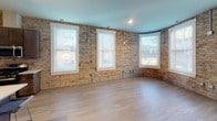 Located at 116 E Hennepin Ave in Minneapolis, this single-floor unit showcases a compelling blend of historic industrial character and contemporary design. Throughout the space, original exposed brick walls in warm golden and red tones serve as a defining architectural feature, providing textural contrast against modern updates and light hardwood flooring that runs through the main living areas.

The open-concept living area is generously proportioned, featuring multiple large windows that flood the space with natural light. A curved brick wall adds architectural interest and a distinctive sense of place. The kitchen is well-appointed with dark espresso cabinetry, white quartz countertops, a subway tile backsplash, stainless steel appliances including a gas range, refrigerator, dishwasher, and microwave, plus a central island with pendant lighting and seating for casual dining.

Bedroom spaces offer a quieter retreat, with carpeted flooring, exposed brick accents, and bright windows. The bathrooms are finished to a high standard, featuring dark wood vanities, white quartz countertops, and sleek backlit mirrors that provide a clean, modern aesthetic. One bathroom also benefits from a window that introduces natural light alongside the exposed brick wall, reinforcing the space's signature character throughout.