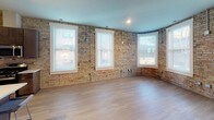 Located at 116 E Hennepin Ave in Minneapolis, this single-floor unit showcases a compelling blend of historic industrial character and contemporary design. Throughout the space, original exposed brick walls in warm golden and red tones serve as a defining architectural feature, providing textural contrast against modern updates and light hardwood flooring that runs through the main living areas.

The open-concept living area is generously proportioned, featuring multiple large windows that flood the space with natural light. A curved brick wall adds architectural interest and a distinctive sense of place. The kitchen is well-appointed with dark espresso cabinetry, white quartz countertops, a subway tile backsplash, stainless steel appliances including a gas range, refrigerator, dishwasher, and microwave, plus a central island with pendant lighting and seating for casual dining.

Bedroom spaces offer a quieter retreat, with carpeted flooring, exposed brick accents, and bright windows. The bathrooms are finished to a high standard, featuring dark wood vanities, white quartz countertops, and sleek backlit mirrors that provide a clean, modern aesthetic. One bathroom also benefits from a window that introduces natural light alongside the exposed brick wall, reinforcing the space's signature character throughout.