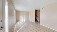 This two-story, 3-bedroom, 2-bathroom home presents a practical and well-organized layout across two levels. The main living area features large tile flooring that reflects natural light streaming in through generous windows fitted with blinds, creating a bright and welcoming atmosphere. A textured ceiling and neutral beige walls provide a clean, understated backdrop throughout. A carpeted staircase with a wood railing connects the two floors seamlessly.

The kitchen is equipped with dark cabinetry, granite-style laminate countertops, a double stainless steel sink, and a dishwasher, offering ample workspace and storage. One of the tiled rooms features a sliding glass door with vertical blinds and a ceiling fan with a light fixture, providing both indoor-outdoor access and comfortable air circulation.

The bedrooms are carpeted and include ceiling fans and windows that bring in natural light. Closet space is provided in each room for added convenience. The bathrooms feature tile flooring, white cabinetry with dark countertops, large mirrors, and Hollywood-style vanity lighting. One bathroom includes a private water closet for added functionality. Throughout the home, the consistent neutral color palette and tile flooring create a cohesive and easy-to-maintain living environment.