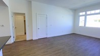 This single-floor space presents a fresh, modern aesthetic defined by crisp white walls and warm wood-look luxury vinyl plank flooring that runs seamlessly throughout. The interior is bright and open, with a clean, minimalist design that offers maximum flexibility for furnishing and personalization. The main living area is generously proportioned, providing ample room for a variety of layout configurations. White baseboards frame the perimeter of each room, adding a polished, cohesive finish to the space. Interior doors feature classic panel detailing and are finished in white to complement the overall palette. An open doorway connects the main living area to an adjacent room, enhancing the sense of flow and connectivity throughout the floor plan. The neutral color scheme and consistent flooring create a unified, welcoming ambiance from room to room. The space appears newly finished or freshly renovated, with clean surfaces and updated materials throughout. Its straightforward, functional design makes it well-suited for a range of uses, offering a versatile foundation that can be easily adapted to suit individual needs and preferences.