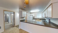 This single-floor residence is thoughtfully designed to maximize functionality and comfort throughout its layout. The kitchen serves as a central hub, featuring white cabinetry with wood-tone trim, dark laminate countertops, and a full suite of white appliances including an electric range, built-in microwave, refrigerator, and dishwasher. A peninsula with matching countertops extends into the adjacent dining and living area, creating an open, connected flow between spaces. A ceiling fan overhead adds to the casual, practical character of this area.

The living room is a generously sized, light-filled space anchored by a tile-surround fireplace and a large picture window that invites natural light and outdoor views. Neutral carpet runs throughout the main living areas, contributing to a warm, cohesive atmosphere. A door provides direct access to an outdoor space.

The bedrooms are comfortable and well-proportioned, each featuring carpet flooring, baseboard heating, and closet storage. The bathrooms include vanities with extended countertops, large mirrors, and tile flooring that adds a practical, clean aesthetic. The overall design is straightforward and functional, with a neutral palette throughout.