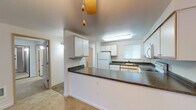 This single-floor residence is thoughtfully designed to maximize functionality and comfort throughout its layout. The kitchen serves as a central hub, featuring white cabinetry with wood-tone trim, dark laminate countertops, and a full suite of white appliances including an electric range, built-in microwave, refrigerator, and dishwasher. A peninsula with matching countertops extends into the adjacent dining and living area, creating an open, connected flow between spaces. A ceiling fan overhead adds to the casual, practical character of this area.

The living room is a generously sized, light-filled space anchored by a tile-surround fireplace and a large picture window that invites natural light and outdoor views. Neutral carpet runs throughout the main living areas, contributing to a warm, cohesive atmosphere. A door provides direct access to an outdoor space.

The bedrooms are comfortable and well-proportioned, each featuring carpet flooring, baseboard heating, and closet storage. The bathrooms include vanities with extended countertops, large mirrors, and tile flooring that adds a practical, clean aesthetic. The overall design is straightforward and functional, with a neutral palette throughout.