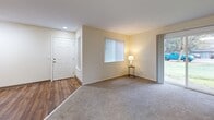 Located in Beaverton, Oregon, this single-floor, two-bedroom, two-bathroom residence offers a practical and comfortable layout. The living room welcomes you with warm-toned carpet, a front entry door, and a large window fitted with vertical blinds that fills the space with natural light. A sliding glass door leads directly outside, providing easy outdoor access and views of the surrounding greenery. The living area transitions into the combined dining room and kitchen, where wood-style flooring, white cabinetry, and standard appliances create a functional cooking and dining space. A ceiling fan adds comfort to the adjoining area. The primary bedroom is generously sized and features plush carpeting, access to a private bathroom, and a walk-in closet with built-in shelving. The second bedroom also features carpet flooring, a window with vertical blinds, and a baseboard heating unit. Both bathrooms include vanities with countertops and full tub-shower combinations with tile surrounds and hardwood-style flooring. Three closets throughout the unit provide ample storage. A dedicated laundry area adds convenience. Neutral wall tones and consistent finishes throughout create a cohesive, move-in-ready aesthetic.