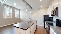 This 2-bedroom, 1-bathroom unit at 805 E Wheeling St in Lancaster, Ohio offers a thoughtfully designed single-floor layout with modern finishes throughout. Light-toned luxury vinyl plank flooring runs continuously across all rooms, creating a cohesive and clean aesthetic. Exposed industrial-style ductwork adds a distinctive architectural character to the living spaces and bedrooms.

The kitchen is well-appointed with crisp white cabinetry extending to the ceiling for generous storage, dark countertops, black appliances including a full-size refrigerator, electric range, and built-in microwave, along with a peninsula that provides additional prep space and seating potential.

The primary bedroom is generously sized, featuring tall ceilings, exposed ductwork, and access to a dedicated closet with wire shelving systems that maximize storage efficiency. The second bedroom is a comfortable, well-lit room with a large window offering natural light and outdoor views. Both bedrooms are finished with neutral tones that complement the flooring.

The bathroom is clean and functional, featuring a full tub-shower combo, a vanity with countertop storage, and matching LVP flooring. A hallway connects the rooms efficiently, and two closets throughout the unit provide ample storage for everyday living.