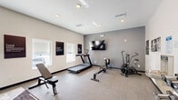 Located in Wildwood, Florida, this fitness center is a purpose-built exercise facility designed to support a full range of workout routines. The space is thoughtfully organized across a single floor, offering a comfortable and functional environment for both cardio and strength training.

One area of the facility is anchored by a multi-function cable and pull-up rack, accompanied by a full set of kettlebells and a weight bench. Floor-to-ceiling mirrors line one wall, visually expanding the space and allowing users to monitor their form. A workout mat on the floor adds a dedicated zone for stretching or floor exercises.

The cardio section features a treadmill, a rowing machine, and an air resistance bike, all positioned beneath a wall-mounted flat-screen television. Motivational wall art with phrases like "Grind," "Execute," and "Hustle" reinforces an energetic atmosphere throughout the room. Natural light filters in through several windows, lending the space a bright and open feel.

Additional amenities include a built-in water fountain, a dumbbell rack with a full set of free weights, and recessed ceiling lighting. The neutral-toned walls, grey accents, and durable speckled flooring contribute to a clean, modern aesthetic. A window pass-through connects to an adjacent area, and a door provides direct access to an outdoor pool area, adding convenience for those enjoying the broader amenity offerings of the community.