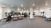 This state-of-the-art fitness center, located at 1001 Blossom Hill Rd in San Jose, CA, is a single-story facility spanning 750 square feet. The space is designed to accommodate a variety of exercise needs with its comprehensive array of equipment. The room features a clean, modern aesthetic with white tiled walls and a durable gray floor, ideal for high-traffic gym use. Bright, recessed lighting fixtures are evenly distributed across the ceiling, ensuring excellent visibility throughout the space.

The gym is equipped with a diverse range of fitness machines, including treadmills, weight training stations, and cardio equipment. Large mirrors line the walls, allowing users to monitor their form during workouts. The layout is well-organized, with clear pathways between equipment for easy navigation. Climate control is evident with the presence of air conditioning units, ensuring a comfortable environment year-round.

Natural light enters through windows along one wall, providing a connection to the outside environment. The facility also includes essential amenities such as water fountains and waste receptacles. Overall, this fitness center offers a functional and inviting space for individuals seeking a comprehensive workout experience.