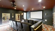 Located at 750 Summer St in Stamford, Connecticut, this single-floor space is home to a dedicated private theater room that delivers an immersive cinematic experience. The theater is designed with careful attention to atmosphere and functionality, featuring deep charcoal-toned walls that absorb light and enhance on-screen visuals. A rich, warm-hued ceiling adds depth and contrast to the room, while recessed lighting provides subtle, controllable illumination throughout. The centerpiece of the space is a large, wall-mounted projection screen paired with a ceiling-mounted projector, creating a true big-screen viewing environment. Rows of plush, high-back leather recliner chairs are arranged in a tiered layout, ensuring clear sightlines from every seat. A raised platform at the rear of the seating area further enhances the theater-style configuration. Classic movie posters adorn the walls, reinforcing the cinematic theme and adding a touch of personality to the space. A patterned area rug anchors the seating area and contributes to the room's sound-dampening qualities. Overall, this space is purpose-built for entertainment, combining professional-grade audiovisual infrastructure with comfortable, stylish furnishings to create an exceptional private screening room.