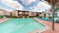 Located at 2700 Westridge St in Houston, Texas, this outdoor communal space centers around a generously sized swimming pool with clear turquoise water, designed to serve the residents of the surrounding multi-story brick buildings. The pool deck is finished in a terracotta-toned surface and is outfitted with vibrant teal lounge chairs and additional seating, providing ample space for relaxation and recreation under the open Texas sky.

A covered pergola structure on one side of the pool area offers a shaded retreat, furnished with seating and positioned near an outdoor grill, making it well-suited for casual gatherings. The perimeter of the pool is enclosed by a black metal fence, with lush shrubs and mature trees — including magnolias and crape myrtles — lending natural greenery and seasonal color to the setting.

The surrounding residential buildings feature a classic brick exterior with balconies accessible from upper-level units, creating an intimate courtyard-like atmosphere around the pool. The layout of the outdoor space, as revealed in the 3D scan, forms a broad open-air area integrated within the residential complex. Overall, the space offers a functional and inviting outdoor amenity area suited for warm Houston weather.