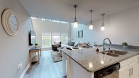 Located at 3930 S Lake Dr in St. Francis, Wisconsin, this two-floor residence offers a thoughtfully designed open-concept layout that seamlessly connects the kitchen, dining, and living areas. The main living space is defined by dramatic soaring ceilings with clerestory windows that flood the room with natural light, complemented by light hardwood-style flooring throughout. A large granite-topped kitchen island serves as the centerpiece, illuminated by a trio of pendant lights and accommodating bar seating for casual dining. The kitchen is fully equipped with stainless steel appliances, white shaker cabinetry, and granite countertops, providing ample storage and workspace. The open living area features large windows that bring in generous natural light and views of the surrounding neighborhood. A bright, carpeted staircase with a sleek handrail connects the two floors, bathed in natural light from an adjacent window. The upper level houses the bedrooms, each finished with plush carpet, multiple windows, and neutral tones that create a calm and restful atmosphere. The bathroom is clean and modern, featuring white cabinetry with stone-look countertops and a tub-shower combination. Throughout the residence, the consistent use of neutral tones and quality finishes creates a cohesive and contemporary living environment.
