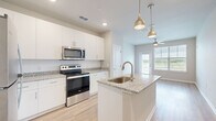 This single-floor residence offers a thoughtfully designed layout with two bedrooms and two bathrooms. The open-concept kitchen and living area serves as the heart of the home, featuring a central island with a granite countertop and integrated sink, white shaker cabinetry, stainless steel appliances, and warm pendant lighting. Light wood-look flooring flows seamlessly throughout the main living areas, complementing the clean, contemporary aesthetic.

The living room is bright and welcoming, benefiting from large windows fitted with white blinds and a glass-paneled door that frames outdoor views and invites natural light deep into the space. A ceiling fan overhead adds both function and style.

The two bedrooms are carpeted for comfort, with the primary bedroom featuring a window for natural light and a convenient en-suite connection. Both bathrooms are finished consistently, each offering a tub-shower combination with white tile surround, granite-topped vanities, and light wood flooring that ties the space together.

Throughout the residence, a neutral color palette of soft whites and warm beige tones creates a calm, cohesive ambiance. The combination of modern finishes, practical layout, and ample natural light makes this a comfortable and functional living space.