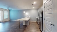 Located at 646 W Smith St in Orlando, FL, this modern single-story unit offers a thoughtfully designed open-concept layout with contemporary finishes throughout. The kitchen is a standout feature, boasting a large island with an extended white quartz countertop, stainless steel appliances including a refrigerator, range, and microwave, white shaker-style cabinetry with brushed nickel hardware, a subway tile backsplash, and globe pendant lighting. Rich wood-look flooring flows seamlessly through the kitchen and living areas, which are accented by cool blue-gray walls that add a modern, airy feel. The living area is generously proportioned, featuring a ceiling fan and sliding glass doors that open to a private balcony, allowing for natural light and outdoor access. The bedrooms are carpeted for comfort, with one room offering direct balcony access. A spacious walk-in closet provides ample storage. The bathroom features a dual-sink vanity with white quartz countertops, gray cabinetry, wood-look flooring, a large mirror, and panel-style doors with brushed nickel hardware. Recessed lighting and clean architectural lines throughout give this unit a fresh, modern aesthetic well-suited for contemporary living in the heart of Orlando.