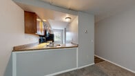 Located at 34 N Shore Cir in Rochester, NY, this multi-floor home spans three levels and offers a practical, well-organized layout with two bedrooms and two full bathrooms. The entry level welcomes you with a closet conveniently positioned near the front door, leading into the main living areas. The open-concept kitchen and dining area features warm wood cabinetry, granite-look countertops, a peninsula with a built-in sink, and black appliances, all opening toward a naturally lit dining space with a window view. The living room provides a comfortable, carpeted gathering space with neutral gray walls that carry throughout the home. Both bedrooms are carpeted and finished with the same soft gray tones, each benefiting from natural light through windows with outdoor views. The bathrooms include wood-vanity cabinetry, white countertops, wood-look vinyl flooring, and tub-shower combinations with bright overhead lighting. Multiple closets across the floors provide ample storage. The unfinished basement offers generous additional space with a concrete floor, exposed ceiling joists, utility systems including a water heater, and staircase access — ideal for storage or future finishing. The home's multi-floor design is connected by several staircases, ensuring easy navigation throughout.