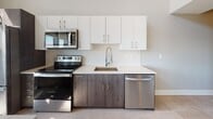 This two-story unit at 1685 Elmwood Ave in Buffalo's Elmwood Village neighborhood showcases a thoughtfully designed interior with modern finishes throughout. The main level impresses immediately with soaring vaulted ceilings and a dramatic wall of large multi-pane windows that flood the space with natural light and offer open views of the surrounding neighborhood. The tile flooring on this level adds a clean, polished look that complements the bright, airy atmosphere.

The kitchen is well-appointed with two-tone cabinetry — crisp white upper cabinets paired with wood-grain lower cabinets — accented by a subtle tile backsplash and light quartz countertops. Stainless steel appliances, including a range, over-the-range microwave, and dishwasher, complete the functional setup.

A striking dark wood horizontal-rail staircase leads to the upper level, where light hardwood flooring runs throughout an open loft-style landing area. Multiple white panel doors provide access to bedrooms and closets, including a generously sized walk-in closet with built-in wire shelving.

The bathrooms are finished with warm-toned tile flooring, floating wood-grain vanities, quartz countertops, and illuminated mirrors. One bathroom features a glass-enclosed tiled shower, delivering a clean, contemporary aesthetic consistent with the rest of the space.