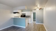 This single-floor unit combines thoughtful design with practical functionality across a compact, efficiently arranged layout. The open-concept living and kitchen area forms the heart of the space, where warm wood-look flooring flows seamlessly underfoot and a ceiling fan provides both comfort and light. A large front window and entry door allow generous natural light to fill the living area, creating a bright and welcoming atmosphere.

The kitchen is designed for efficiency, featuring a galley-style configuration with white shaker cabinetry, light stone-patterned countertops, and a classic subway tile backsplash. Black appliances — including a range and refrigerator — provide a bold contrast to the crisp white cabinetry. A peninsula with a light blue accent wall separates the kitchen from the living space, adding a pop of color while offering additional counter space. A range hood overhead completes the cooking area.

The bathroom is clean and functional, outfitted with white cabinetry, a vanity with matching countertops, a toilet, and a shower-tub combination. The bedroom benefits from dual side-by-side closets with hanging rods, offering ample storage. Throughout the unit, consistent wood-look flooring, neutral gray wall tones, and white trim create a cohesive, modern aesthetic.