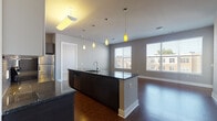 Located at 23220 Chagrin Blvd in Beachwood, Ohio, this single-floor residence offers a thoughtfully designed open-concept layout with modern finishes throughout. The kitchen serves as a central hub of the space, showcasing a large island with a dark granite countertop, an integrated sink, and pendant lighting suspended overhead. Stainless steel appliances, including a full-sized refrigerator, complement the two-tone cabinetry — white upper cabinets contrasted by dark lower units — and a metallic tile backsplash adds a contemporary accent. Rich hardwood flooring flows through the main living and kitchen areas, creating a warm and cohesive aesthetic. The spacious living area benefits from an abundance of natural light through multiple large windows with views of the surrounding community. Bedrooms feature plush wall-to-wall carpeting and windows that provide natural light. The bathrooms are finished with large-format tile flooring, dark wood vanities topped with granite countertops, tile-surround showers, and dedicated walk-in closet access. A half bath provides added convenience. The overall design palette of neutral grays and warm wood tones creates a clean, modern ambiance throughout this well-appointed space.
