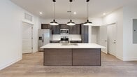 This single-story, 3-bedroom, 2-bathroom home offers a thoughtfully designed open-concept layout with modern finishes throughout. The heart of the home is the combined kitchen and living area, where a large center island with a white quartz countertop and undermount sink serves as the focal point. Three sleek pendant lights hang above the island, complementing the dark espresso cabinetry that lines the kitchen walls. Stainless steel appliances, including a refrigerator with ice maker, range, and microwave, complete the kitchen. Light wood-look flooring flows throughout the main living areas, creating a clean and cohesive aesthetic against the crisp white walls. The primary bedroom is generously sized and includes dedicated closet space. The two additional bedrooms feature neutral carpet, ceiling fans, and windows that allow natural light to fill each room. Both bathrooms are finished with dark wood vanities, white countertops, and light wood-look flooring, maintaining a consistent design language. A dedicated laundry room houses a full-sized, side-by-side washer and dryer with overhead wire shelving for added storage. Three closets provide ample storage throughout the home, rounding out this well-equipped and move-in-ready residence.