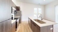Located at 2427 Quincy Ave in Ogden, Utah, this modern 1-bedroom, 1-bathroom apartment offers 500 square feet of thoughtfully designed single-floor living space. The open-concept layout seamlessly connects the living room, dining area, and kitchen, all unified by light-toned hardwood-style flooring and crisp white walls that enhance the sense of space and brightness. The contemporary kitchen is a standout feature, centered around a large island with a white quartz countertop, an undermount stainless steel sink, and dark wood cabinetry. It is fully equipped with stainless steel appliances, including a refrigerator, range, microwave, and dishwasher. Natural light flows generously through vertical blinds and large windows, with views of the surrounding mountains visible from the bedroom. The 120-square-foot primary bedroom is a clean, airy retreat with light flooring and a dedicated closet. The bathroom features a full tub/shower combo with a white surround, a wood-toned vanity with quartz countertop, and matching light flooring. A programmable thermostat and ceiling fan add practical comfort throughout. The unit's modern, minimalist aesthetic and efficient layout make it an ideal living space in Ogden.