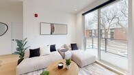 Located at 10318 116 St in Edmonton's vibrant Oliver neighbourhood, this thoughtfully designed 2-bedroom, 3-bathroom unit offers a clean, contemporary aesthetic across its single floor. Light hardwood flooring runs throughout, complementing the all-white walls and creating a bright, cohesive atmosphere.

The kitchen is a standout feature, showcasing a U-shaped layout with warm wood lower cabinetry, crisp white upper cabinets, white quartz countertops, and a full suite of stainless steel appliances including a French door refrigerator, over-the-range microwave, and dishwasher. A kitchen island provides additional counter space and seating.

The living room is bathed in natural light, with floor-to-ceiling sliding glass doors opening onto a private balcony that offers views of the surrounding neighbourhood's mature trees and streetscape.

The primary bedroom is generously proportioned, featuring corner windows that flood the room with natural light and a wall-mounted television. A walk-in closet with built-in shelving leads directly to an ensuite bathroom. The second bedroom also includes a window with outdoor views and a wall-mounted TV. All three bathrooms maintain the minimalist design language, with white tile, wood-accented vanities, and large mirrors.