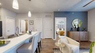 This thoughtfully designed 1-bedroom, 1-bathroom unit offers an efficient and stylish single-floor layout. The open-concept kitchen, dining, and living area forms the heart of the unit, where warm wood-look flooring flows throughout. The kitchen is outfitted with rich dark cabinetry, a subway tile backsplash, black appliances, and a generous white quartz peninsula with bar seating — ideal for both meal prep and casual dining. Pendant lighting above the peninsula adds a modern touch.

The living room features a ceiling fan, large glass French doors that invite natural light, and direct access to a private balcony. The balcony offers open views of surrounding greenery and is large enough to accommodate outdoor seating.

The spacious primary bedroom includes a ceiling fan, a large window with ample natural light, and a sliding barn door that opens to a dedicated in-unit laundry closet with a stacked washer and dryer. The bathroom features dark wood cabinetry, a white countertop vanity, wood-look flooring, and a full tub-shower combo with tile surround. Neutral tones and clean architectural lines throughout give the space a cohesive, contemporary feel.