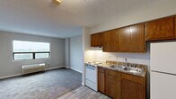 Located at 4700 Westgrove St in Raleigh, NC, this one-bedroom, one-bathroom unit offers a practical and efficiently organized single-floor layout. The living room features neutral-toned carpet flooring, a wall-mounted HVAC unit, and a large window that brings in natural light and outdoor views of the surrounding greenery, creating a comfortable and open atmosphere. The kitchen is positioned adjacent to the living area and is equipped with warm oak cabinetry — both upper and lower — a double-basin sink with a countertop surface, a white electric range with overhead ventilation, and a full-size refrigerator. Light wood-style vinyl flooring runs throughout the kitchen, complementing the cabinetry tones. The bedroom is a well-proportioned space with plush carpet, a broad window with outdoor views, a wall HVAC unit, and a dedicated closet with a hanging rod. A separate closet space features wire shelving on both sides and houses the water heater. The bathroom includes a full tub-shower combo, a toilet, and a single vanity sink, finished with light tile flooring and neutral wall tones. A textured ceiling is present throughout the unit, and a utility panel is accessible from the living area.