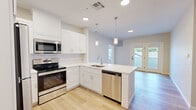 This thoughtfully designed single-floor residence offers three bedrooms and one bathroom within a compact, efficiently organized layout. Light hardwood flooring runs consistently throughout the space, creating a warm and cohesive aesthetic from room to room.

The kitchen is a standout feature, boasting crisp white shaker cabinetry, white quartz countertops, and a full suite of stainless steel appliances including a refrigerator, electric range with microwave, and dishwasher. A peninsula with pendant lighting adds both function and style, while French doors at the rear provide natural light and outdoor access.

The three bedrooms are finished in neutral tones with light hardwood flooring and windows that invite natural light and views of the surrounding neighborhood. The primary bedroom includes a dedicated closet area with wire shelving for organized storage. Additional bedrooms feature clean-panel white doors with matte black hardware, including a double-door closet configuration in one room.

The bathroom is finished with light tile flooring and includes essential fixtures with clean, simple detailing. A connecting hallway links the rooms with ease. Throughout, the space maintains a fresh, modern character with neutral wall tones, white trim, and consistent finishes that create a bright and welcoming atmosphere.