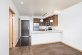 This single-floor residence offers a thoughtfully designed layout that balances style and functionality. The kitchen serves as the heart of the space, showcasing rich, warm-toned wood cabinetry paired with granite countertops that extend across a peninsula breakfast bar — ideal for casual dining or meal prep. A full suite of stainless steel appliances includes an electric range, built-in microwave, refrigerator, and dishwasher. Pendant lighting above the peninsula adds a refined touch, while track lighting overhead ensures ample illumination throughout the cooking area. Durable hardwood-style flooring grounds the kitchen and flows into the adjoining living area, creating a cohesive open feel. The bedroom is finished with plush wall-to-wall carpeting, warm wood baseboards, and a window that brings in natural light and offers a glimpse of the surrounding neighborhood. The bathroom features a granite-topped vanity with an undermount sink, a large frameless mirror, and clean, neutral finishes throughout. Overall, the space presents a modern yet comfortable aesthetic, with consistent use of granite and wood tones tying each room together into a harmonious and inviting interior.