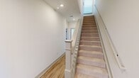This well-appointed three-story home in Huntsville, Alabama offers four bedrooms, five bathrooms, and a thoughtfully designed layout spread across three distinct floors. The ground level houses an attached garage with a contemporary glass-panel door, an electrical panel, and direct interior access via carpeted staircases with clean white railings and wood-look flooring in the stairwells. The main living floor serves as the heart of the home, featuring an open-concept kitchen and living area. The kitchen is equipped with two-tone wood cabinetry, a large center island with a dark stone countertop, stainless steel appliances, and modern pendant lighting — all anchored by warm hardwood-style flooring. The upper floor hosts the bedrooms, including a generously sized primary suite with plush carpeting, a ceiling fan, a wide window offering outdoor views, and a walk-in closet with wire shelving. Bathrooms throughout feature large-format tile surrounds, sleek matte black hardware, wood-toned vanities, and granite countertops. A dedicated laundry room on the upper level includes side-by-side washer and dryer units, a utility shelf, and a bright window. The home's clean, modern aesthetic is consistent throughout, with white walls, recessed lighting, and durable flooring choices that balance style and practicality.