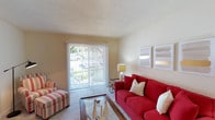 This single-story, 1-bedroom, 1-bathroom residence is thoughtfully laid out to maximize functionality and comfort across its well-proportioned floor plan. The living room serves as the heart of the home, featuring soft carpeting, a textured ceiling, and a full-width sliding glass door fitted with vertical blinds that floods the space with natural light and provides a view of the surrounding greenery outside. The open layout comfortably accommodates both a seating area and a dedicated media zone. Adjacent to the living room, a separate dining area is defined by a chandelier overhead and features louvered bifold closet doors for additional storage. The galley-style kitchen is efficiently designed with white cabinetry, white countertops, and a full suite of appliances including a refrigerator, electric range, and dishwasher, all set on easy-to-maintain flooring. The bedroom is a calm retreat with plush carpeting, a large window with outdoor views, and a full-width closet with louvered bifold doors offering generous storage. The full bathroom is clean and functional, featuring a tub-shower combination, a toilet, and a single-sink vanity with white cabinetry and a mirror. The overall ambiance throughout is light and neutral, with warm beige tones creating a welcoming and cohesive atmosphere.