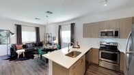 This contemporary two-story residence offers a thoughtfully designed layout with modern finishes throughout. The main level showcases an open-concept kitchen and living area, where a sleek kitchen island with a white quartz countertop and undermount sink serves as the central focal point. Light wood cabinetry pairs with stainless steel appliances, including a range, microwave, and refrigerator, while track lighting and wood-look vinyl flooring add to the modern aesthetic. The kitchen flows seamlessly into a bright dining and living area, where large windows dressed with dark grommet curtains and white blinds invite natural light into the space.

The upper level features multiple bedrooms, each finished with plush neutral carpeting, ceiling fans, and windows that bring in natural light. The bedrooms offer generous proportions and a clean, versatile canvas. The primary bathroom includes a glass-enclosed shower, wood-tone vanity with white countertop, and wood-look flooring. A secondary full bathroom features a shower-tub combination and a matching vanity, maintaining the home's consistent modern style. Clean white walls, consistent trim work, and thoughtful material choices throughout both floors create a cohesive and inviting living environment.