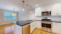 Located at 38 Grove Ave in Cedar Grove, NJ, this well-appointed two-story home offers 2 bedrooms and 3 bathrooms across a thoughtfully designed layout. The main floor, which comprises the larger portion of the home, features warm hardwood flooring throughout the open living and dining areas. The living room impresses with dramatic vaulted ceilings that lend an expansive, airy feel, complemented by natural light from large windows and access to an outdoor area. The modern kitchen is a standout, showcasing white shaker cabinetry, dark countertops, a subway tile backsplash, stainless steel appliances including a gas range, built-in microwave, dishwasher, and refrigerator, as well as pendant lighting and a central island with a sink. The dining area features additional natural light through a large window with a ceiling-mounted drum light fixture. Upstairs, the generous primary bedroom offers plush carpeting, ample natural light, and a large walk-in closet with wire shelving. The second bedroom features vaulted ceiling details and hardwood flooring. The bathrooms are finished with marble countertops, white cabinetry, and brushed nickel fixtures. Two closets and a hallway complete this clean, move-in-ready home.