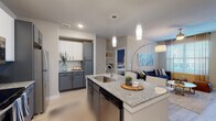 This well-designed single-floor residence offers a cohesive modern aesthetic carried throughout each room. The open-concept kitchen serves as a central feature, showcasing a large granite-topped island with an undermount sink, pendant lighting overhead, and a two-tone cabinet scheme pairing white uppers with slate-gray lowers. Stainless steel appliances, including a refrigerator, range, and built-in microwave, complete the functional workspace. The kitchen flows directly into the living area, which features light wood-style flooring, a ceiling fan, and a glass-panel door providing access to an outdoor balcony and filling the space with natural light.

The unit includes multiple bedrooms, each equipped with ceiling fans, large windows with blinds and draping curtains, and light wood-style flooring. One bedroom features a bold accent wall in deep navy, while another presents a neutral palette. Each bedroom connects to a private bathroom finished with granite-topped vanities, gray cabinetry, and walk-in closets with built-in shelving. The bathrooms also feature soaking tubs and/or shower combinations. A dedicated utility area with laundry hookups adds everyday convenience to this thoughtfully appointed residence.