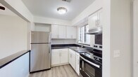 This single-floor unit offers a clean, functional layout with updated finishes throughout. The kitchen is a standout feature, showcasing white shaker-style cabinetry with brushed nickel hardware, dark countertops, and a full suite of stainless steel appliances including a refrigerator, electric range with oven, and a built-in range hood. A single-basin sink sits beneath a window fitted with horizontal blinds, allowing natural light to brighten the space. Light wood-look flooring ties the kitchen together with a fresh, contemporary feel.

The living and sleeping areas are finished with neutral-toned carpet and painted in a soft gray palette, creating a calm, versatile backdrop. Vertical blinds on the windows provide both privacy and light control, while ceiling-mounted light fixtures illuminate each room. The floor plan appears compact yet well-organized, making efficient use of available space.

The bathroom features a tub and shower combination with white subway-style tile, a handheld showerhead, and grab bars for added accessibility. White cabinetry with dark countertops continues the design language from the kitchen, and light wood-look flooring completes the space with a cohesive finish throughout.