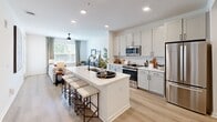 Located at 2020 Winters Eve Dr in Charlotte, NC, this well-appointed one-bedroom, one-bathroom residence offers a thoughtfully designed single-floor layout with a bright, open-concept living space. Light wood-tone flooring runs throughout, complementing the crisp white walls and recessed lighting that create a clean, contemporary ambiance.

The kitchen serves as the heart of the home, anchored by a central island with a white quartz countertop, an undermount sink with a matte black faucet, and seating for casual dining. Stainless steel appliances and two-tone cabinetry with black hardware complete the functional and stylish kitchen design. The space flows seamlessly into the living room, which is bathed in natural light from oversized windows and a glass door leading to a private balcony with outdoor views.

The bedroom is a comfortable retreat featuring a ceiling fan, generous wall space, and direct access to the full bathroom. The bathroom is finished with a dual-sink vanity with white quartz counters, grey cabinetry, matte black hardware, a large mirror with bar lighting, and a tiled soaking tub and shower area. A spacious walk-in closet with wire shelving and an in-unit stacked washer and dryer adds practical convenience to the overall layout.