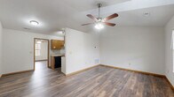 This 2-bedroom, 1-bathroom single-story home offers a practical and comfortable layout with consistent light-toned hardwood-style flooring and neutral walls throughout. The open-concept living, dining, and kitchen area forms the heart of the home, highlighted by a vaulted ceiling with a ceiling fan that enhances the sense of spaciousness and airflow. The kitchen features a galley-style design with warm honey-toned cabinetry lining both sides, light countertops, a double sink, and black appliances including a refrigerator, dishwasher, and range. A pantry door at the end of the kitchen provides convenient additional storage. Both bedrooms are well-proportioned, each equipped with a ceiling fan and a window that allows natural light to filter in. The primary bedroom is notably spacious, with room for a full furniture arrangement. The full bathroom includes a soaking tub-shower combination with a clean, bright surround. Additional functional spaces include a dedicated laundry area, a hallway connecting the rooms, and two closets for ample storage. The home's clean, move-in-ready condition and cohesive design make it a practical and inviting living space.