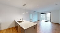 Located in Milwaukee's dynamic East Side neighborhood, this modern 2-bedroom, 2-bathroom unit offers a thoughtfully designed open-concept layout finished with warm hardwood-style flooring and crisp white walls throughout. The kitchen serves as a central hub, showcasing sleek gray cabinetry, stainless steel appliances, a subway tile backsplash, and a generous island with a white quartz countertop and undermount sink — illuminated by a sleek pendant light fixture. The kitchen flows seamlessly into a bright, spacious living room equipped with a wall-mounted mini-split system and large sliding glass doors that open to a private balcony, filling the space with natural light and offering views of the surrounding cityscape. The expansive primary bedroom provides a comfortable retreat, with ample space and easy access to a dedicated bathroom featuring a walk-in shower with sliding glass doors and brushed nickel hardware. The second bedroom is well-proportioned with a large black-framed window offering urban views. A second full bathroom includes a tub-shower combo with a curved curtain rod and matching brushed nickel fixtures. Clean lines, a neutral palette, and modern finishes give this unit a fresh, contemporary ambiance throughout.