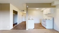 Located at 2175 S Mallul Dr in Anaheim, CA, this efficiently designed studio unit offers a well-organized single-floor layout that makes smart use of every square foot. The open living area is finished with plush neutral carpeting and painted in warm beige tones, creating a bright and welcoming atmosphere. A sliding glass door floods the space with natural light and provides direct access to a private balcony with outdoor views of the surrounding neighborhood.

The kitchen is defined by a peninsula-style counter with a stainless steel sink, white cabinetry, and a white electric range, all finished with wood-look flooring that extends through the hallways. A closet with sliding doors provides convenient built-in storage off the main living area.

The bathroom is clean and functional, featuring wood-look flooring, a full tub and shower combination, a toilet, and a vanity with white cabinetry topped with a speckled stone-style countertop and a large mirror. The textured ceilings are consistent throughout the unit, adding a classic residential character. Two hallways connect the key areas of the unit, contributing to a logical and efficient flow throughout the space.